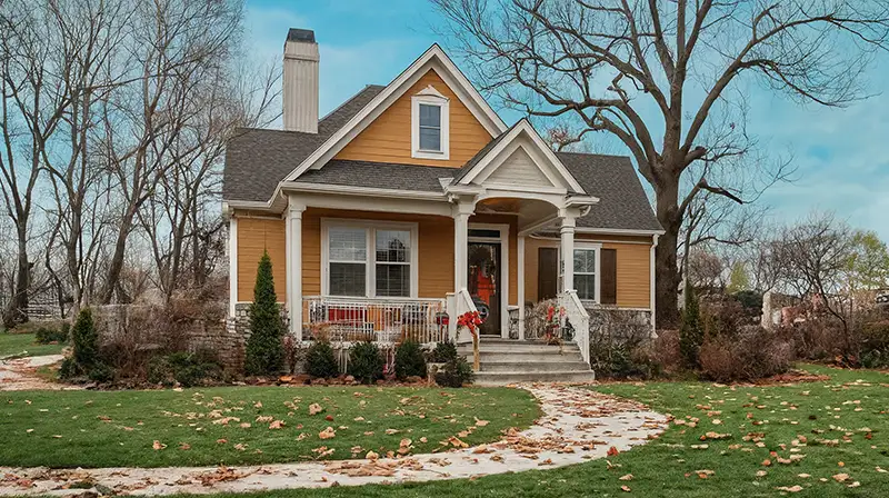 A cozy two-story home painted orange and surrounded by trees during autumn. Winter tree care is important for trees’ overall health.